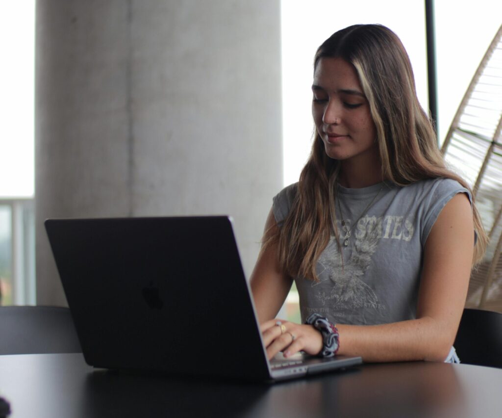 A young woman focused on her laptop, studying in a modern indoor setting.