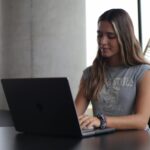 A young woman focused on her laptop, studying in a modern indoor setting.